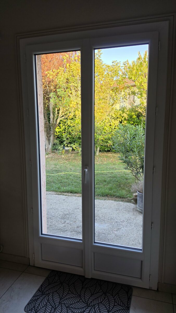 Porte-fenêtre PVC blanc à deux vantaux avec soubassement, vue intérieure sur jardin à Miribel